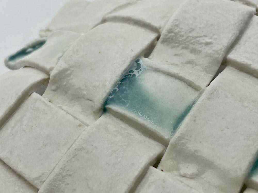 close up of woven strips of porcelain glazed in translucent and blue.