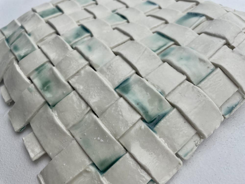 a ceramic sculpture made from woven strips of porcelain, glazed in translucent and blue.