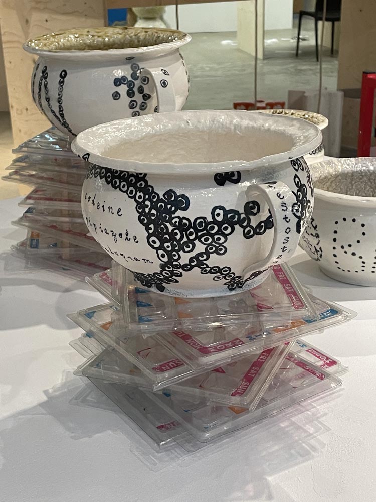 Two porcelain chamber pots perched on piles of dossette boxes on a white surface. Both have underglaze designs of cells.